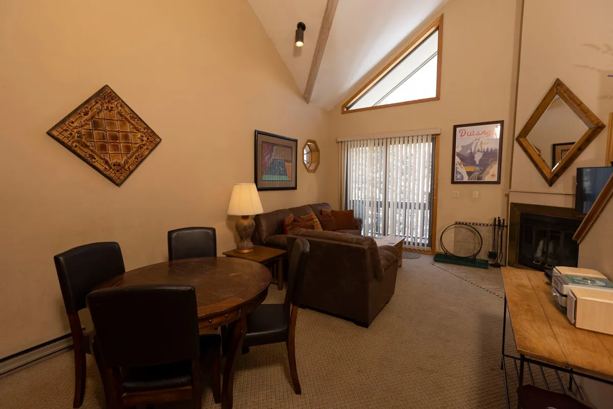 A welcoming dining area seamlessly connected to a spacious living room, complete with a central dining table, sofa, tasteful artwork, and a fireplace. The layout invites family meals, social gatherings, and storytelling in a warm, communal atmosphere.